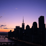 Wide-angle view of silhouetted skyscrapers under an orange-to-blue evening sky.