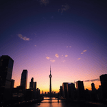 Urban skyline at sunset, tallest tower off-center, shimmering river below.