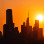 Panoramic city skyline silhouetted against a vivid orange sunset sky.