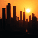 Dramatic silhouette of a city skyline stretched across a fiery sunset gradient.