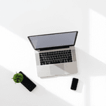 Modern laptop sits alone on a matte white desk in soft daylight.