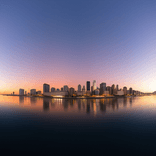 Panoramic view of city buildings silhouetted against an orange twilight sky.