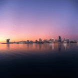 Evening harbor scene with illuminated city lights and pastel reflections.