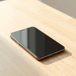 Minimalist black smartphone centered on a pale oak table under soft light.