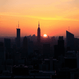 City skyline silhouettes against a dramatic orange and pink sunset sky.