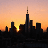 Skyscrapers form dark outlines under a glowing sunset gradient sky.