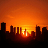 Silhouetted cityscape with rooftop details under a saturated sunset.